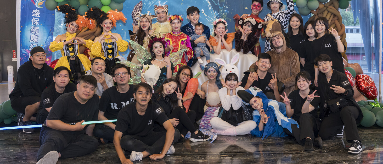 《魔法師的考驗-地球危機!》演出後,穿戲服的演員與穿黑衣的幕後工作人員在演出海報前席地合影