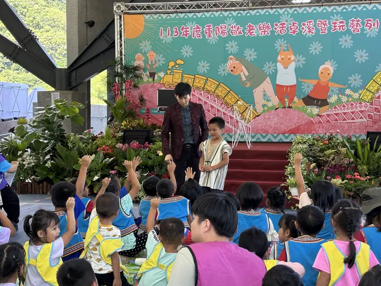 花蓮藝文列車《魔幻兄弟》 演出劇照:戶外舞台場面照:魔術師與原住民服飾小朋友站在彩繪背板前