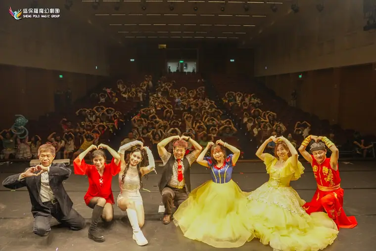 桃園市政府文化局演藝廳《魔幻嘉年華》 演出劇照:全體演員在台前比愛心、身後整場觀眾也一起比愛心