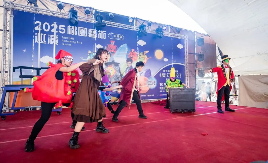 《魔幻時空》桃園大園航空城戶外舞台,演員在「2025 桃園藝術巡演」背板前演出追逐的群戲