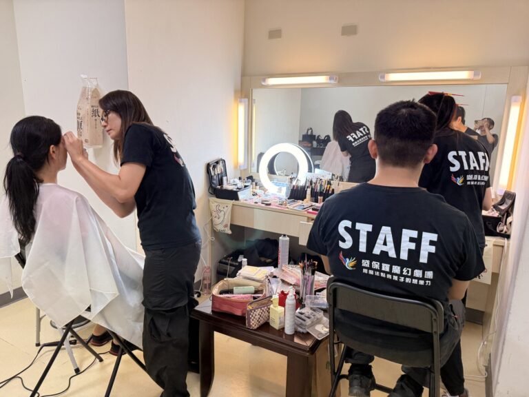 演出前的後台化妝間,彩妝師為演員上妝,穿 STAFF 上衣的工作人員在一旁準備