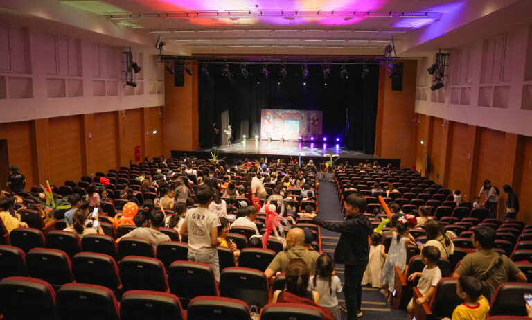 《魔幻嘉年華》桃園市政府文化局演藝廳,從觀眾席後方望向舞台,觀眾手拿造型氣球