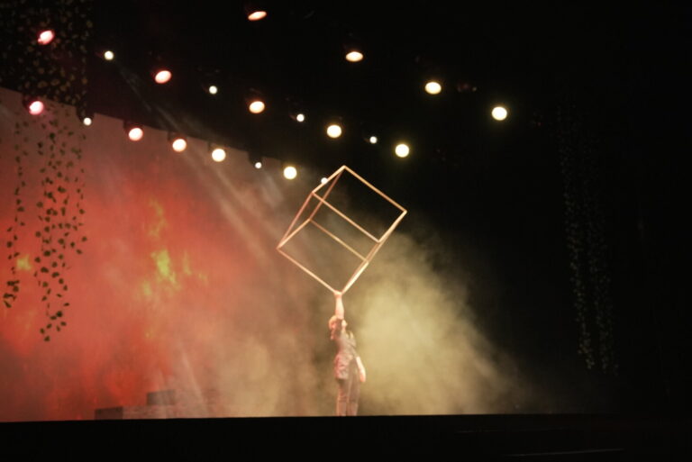 《魔法師的考驗-地球危機!》桃園展演中心展演廳,紅橘色燈光中演員單手頂起大型立方體