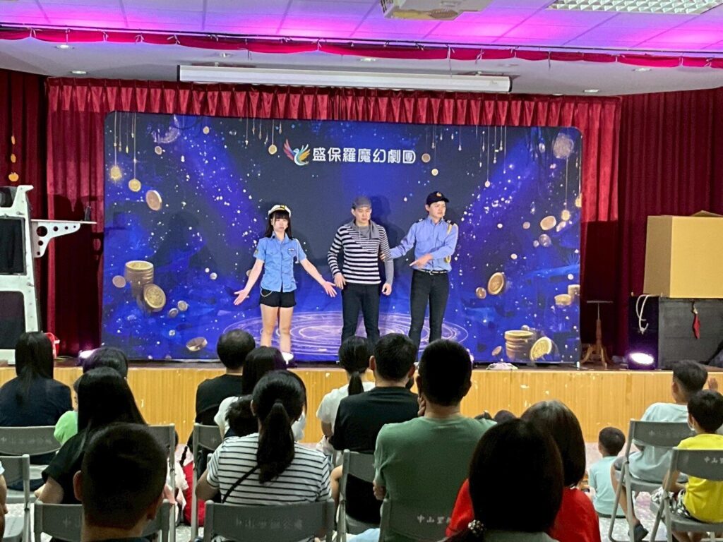 《怪盜神偷》2025 桃園社區藝文巡演,中壢中山市民活動中心舞台上三位演員在劇團背板前演出,前排觀眾背影