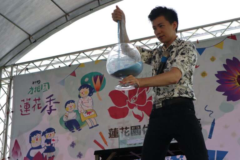 桃園蓮花季魔術秀，魔術師舉起裝彩色沙的玻璃瓶