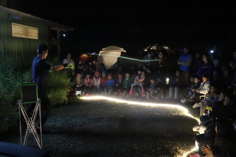 雲起露營區夜間魔術秀，魔術師拋出道具，觀眾圍坐
