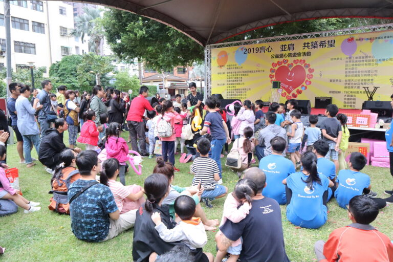 「2019齊心並肩共築希望」公益愛心園遊會魔術表演，草地上坐滿親子觀眾
