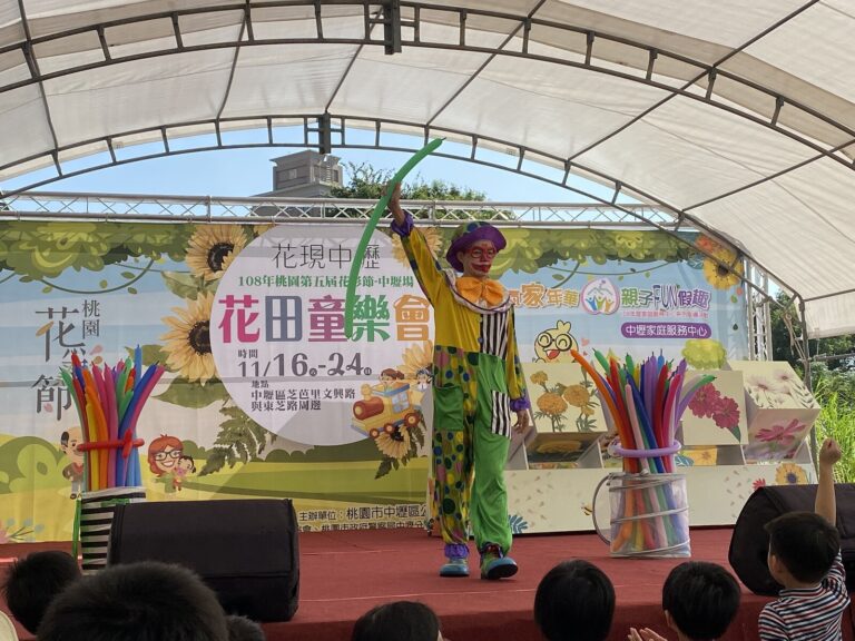 桃園花彩節中壢場《小丑大氣球特技秀》，小丑在「花田童樂會」背板前