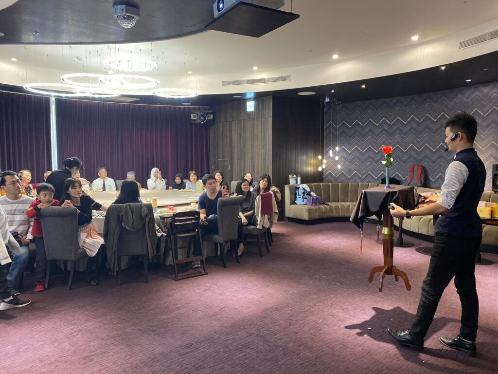 岡原公司新春餐會魔術表演,魔術師在宴會廳表演區,各桌賓客觀看