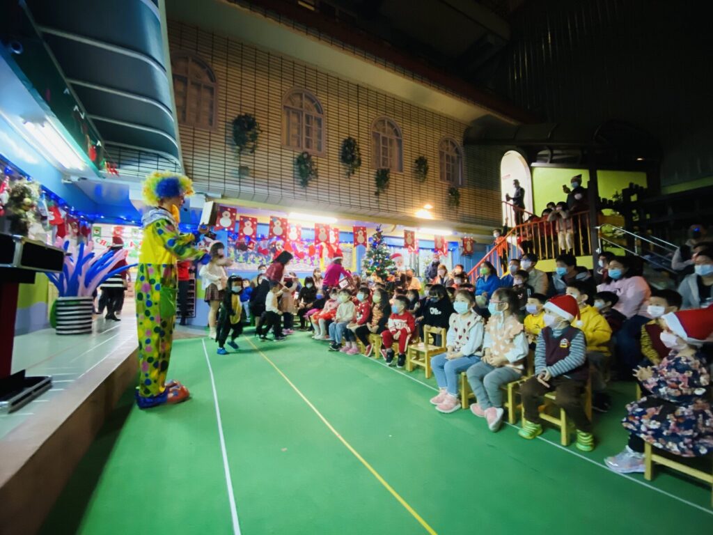 幼兒園聖誕晚會小丑魔術表演,小丑魔術師在場邊,親子坐滿活動場