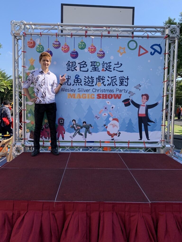 魔術師站在「銀色聖誕之魷魚遊戲派對」學校操場舞台背板前