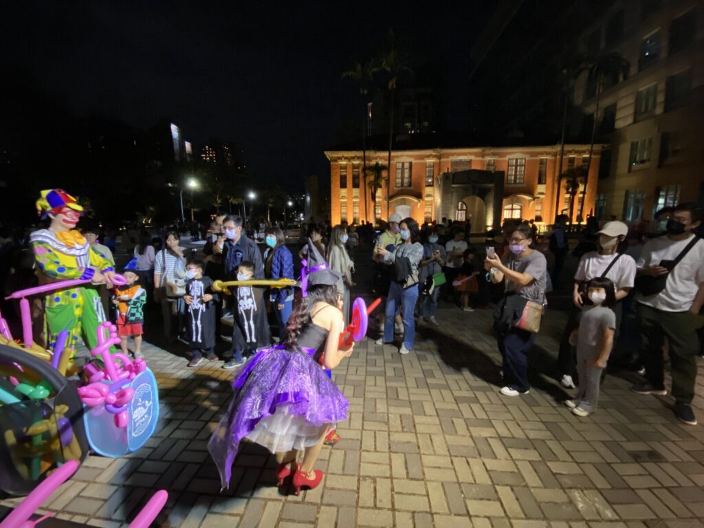 新竹萬聖節活動,小丑與女巫在紅磚建築前做造型氣球,周圍排隊的民眾