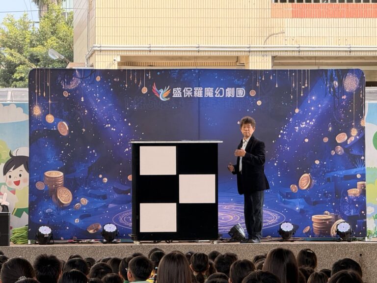 魔術師站在黑白幻術箱旁，豐村國小兒童節魔術演出