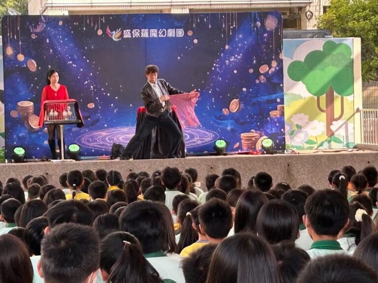 魔術師在豐村國小舞台表演，台下學生背影