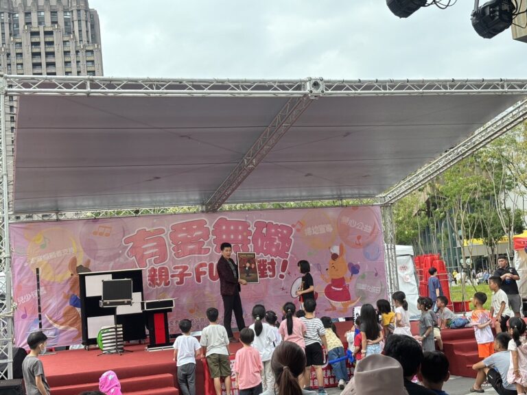 桃園藝文廣場「有愛無礙親子 FUN 派對」舞台全景，背板前的魔術道具與台前觀眾